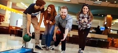 Folk bowler sammen, læner sig frem og ser en grøn bowlingkugle rulle ned ad banen.