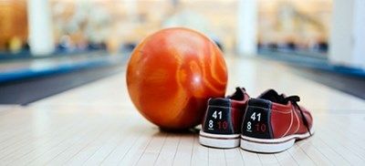 Bowlingkugle og et par sko på en bane med slørede kegler i baggrunden