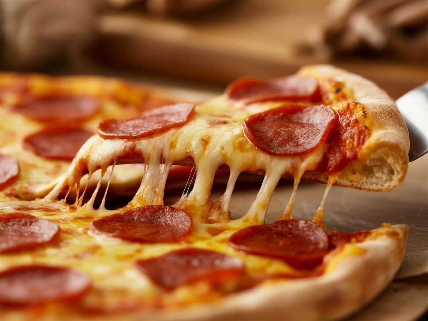 Nærbillede af et stykke pepperoni-pizza, der løftes, med smeltet ost, der strækker sig fra tærten