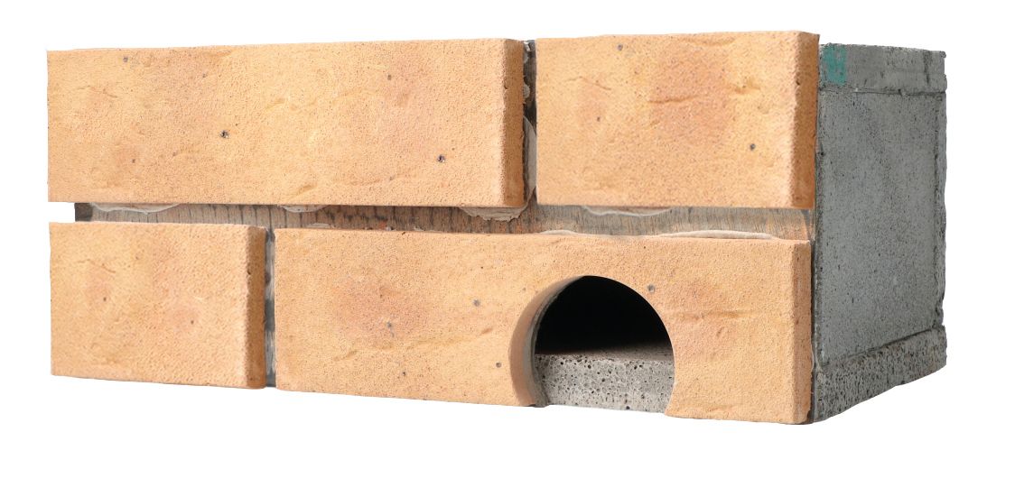 Stacked bricks with a gray cinder block on top, showing a small arch opening in the lower brick layer