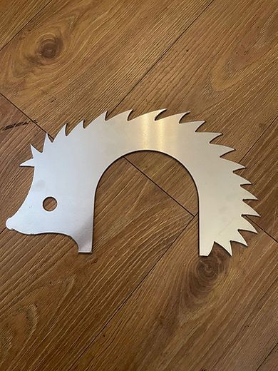 Silver metal hedgehog-shaped cutout with sawtooth spikes on a wooden floor