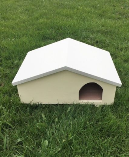 Small white pet house with an arched doorway sitting in green grass.