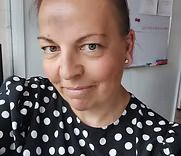 Close-up selfie of a person in a black-and-white polka dot top, smiling slightly indoors