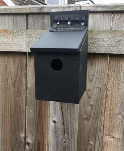Black birdhouse mounted on a wooden fence.