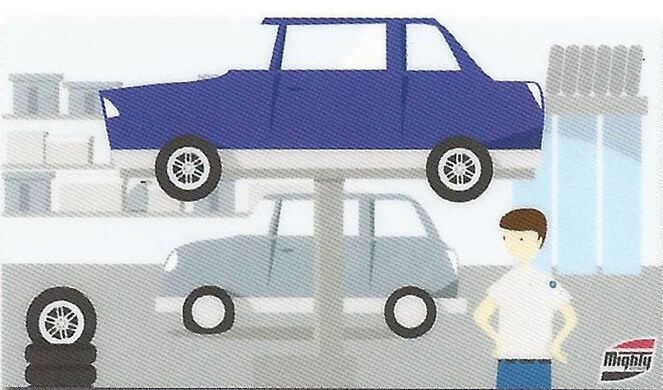 A man is standing in front of a blue car on a lift.