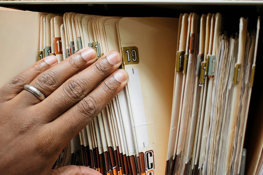 Hand flipping through hanging file folders in a filing cabinet