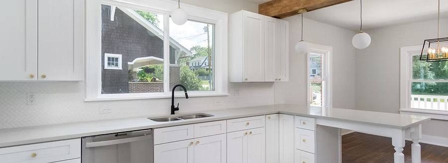 Bright white kitchen with island, sink under window, and pendant lights, in a modern open-plan home