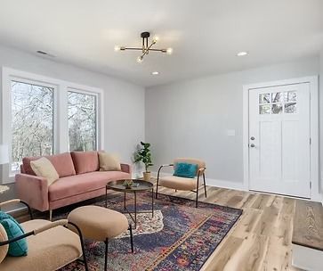 Bright living room with pink sofa, patterned rug, wood floors, and white door and windows.