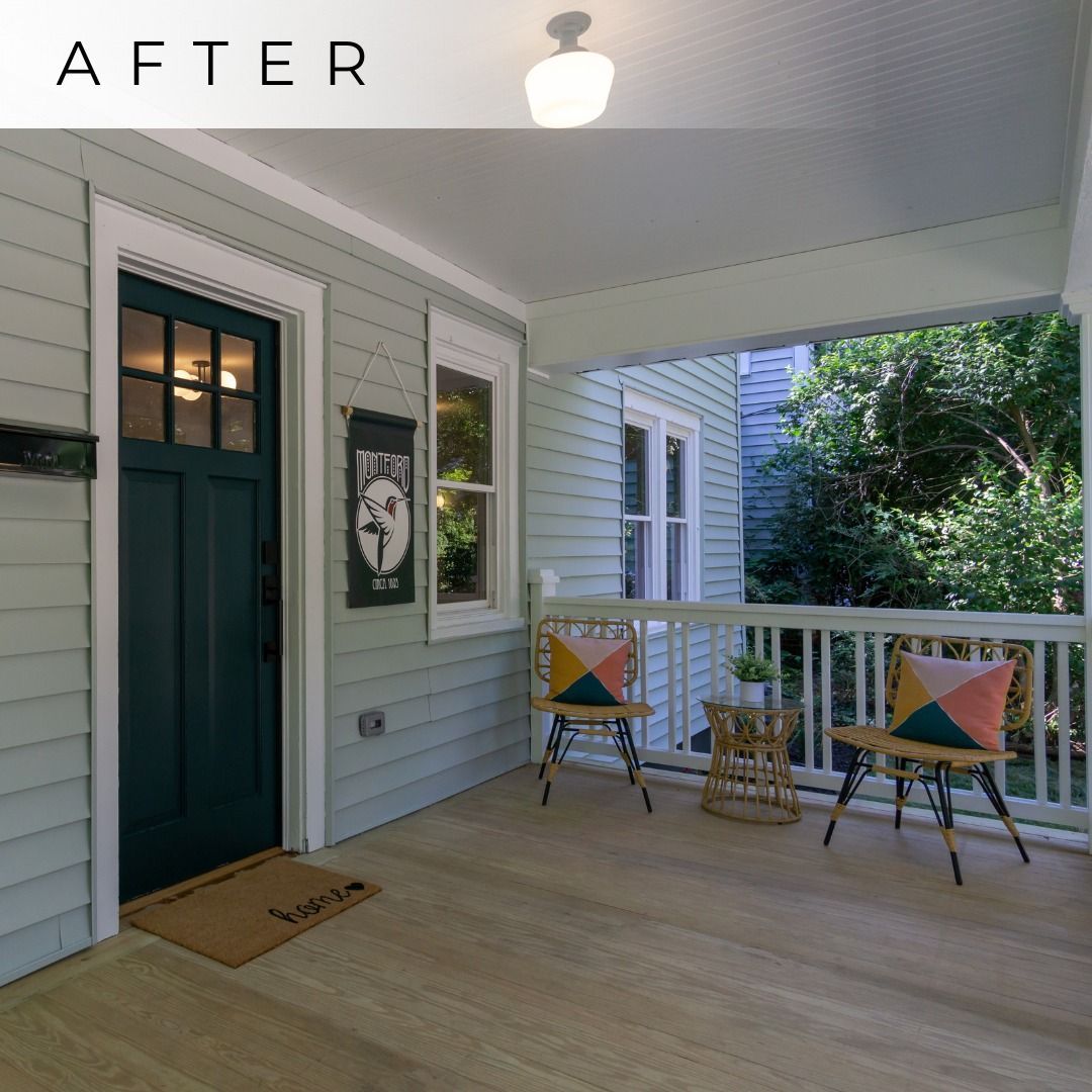 Covered front porch with light wood floor, green door, chairs, and small table beside white siding.
