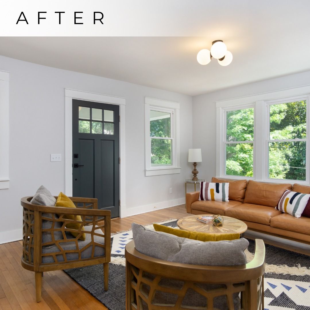 Bright living room with tan sofa, woven chairs, round table, large windows, and a dark front door.