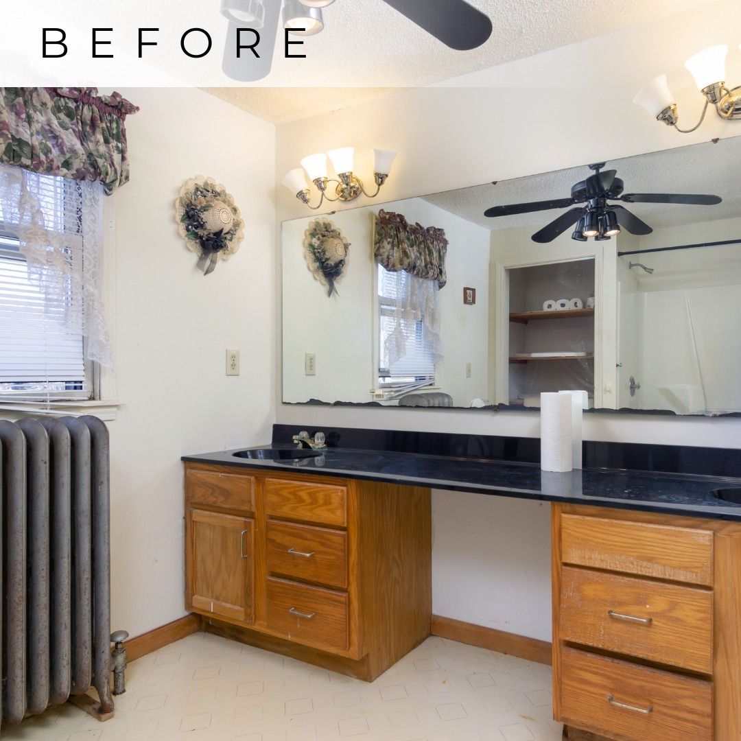Bathroom vanity with black countertop, wood cabinets, large mirror, wall sconces, and a radiator by the window.