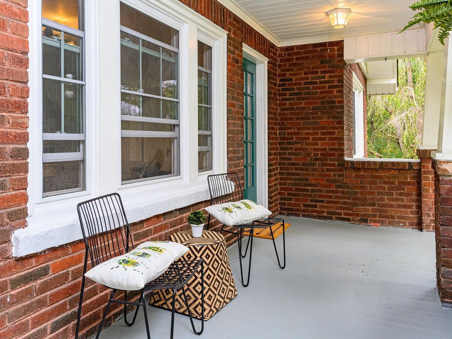 Brick front porch with white windows, two chairs, and a small patterned table on a gray floor