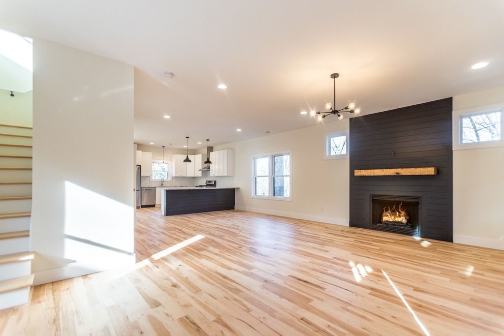 Bright open living room with hardwood floors, kitchen area, and a black stone fireplace with a wooden mantel