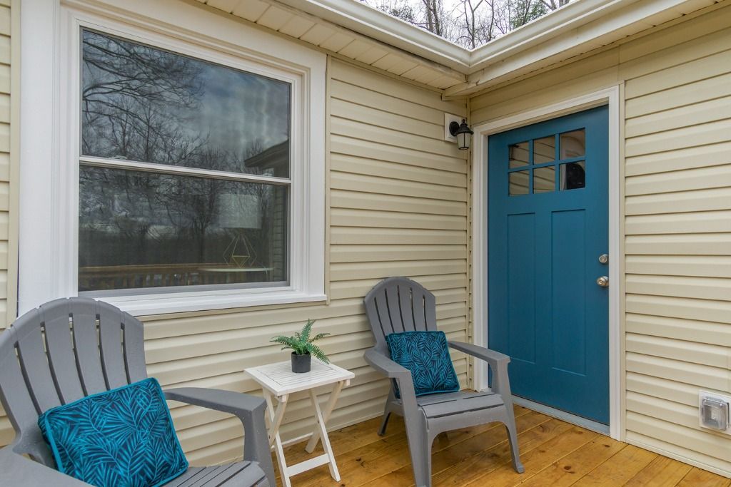 Front porch with two gray chairs, a small white table, a blue door, and beige siding