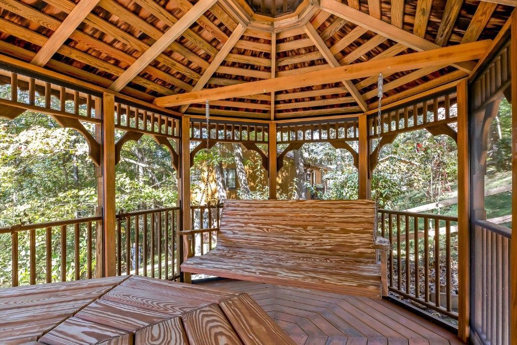 Open-air wooden gazebo with a woven roof and bench, surrounded by lush greenery