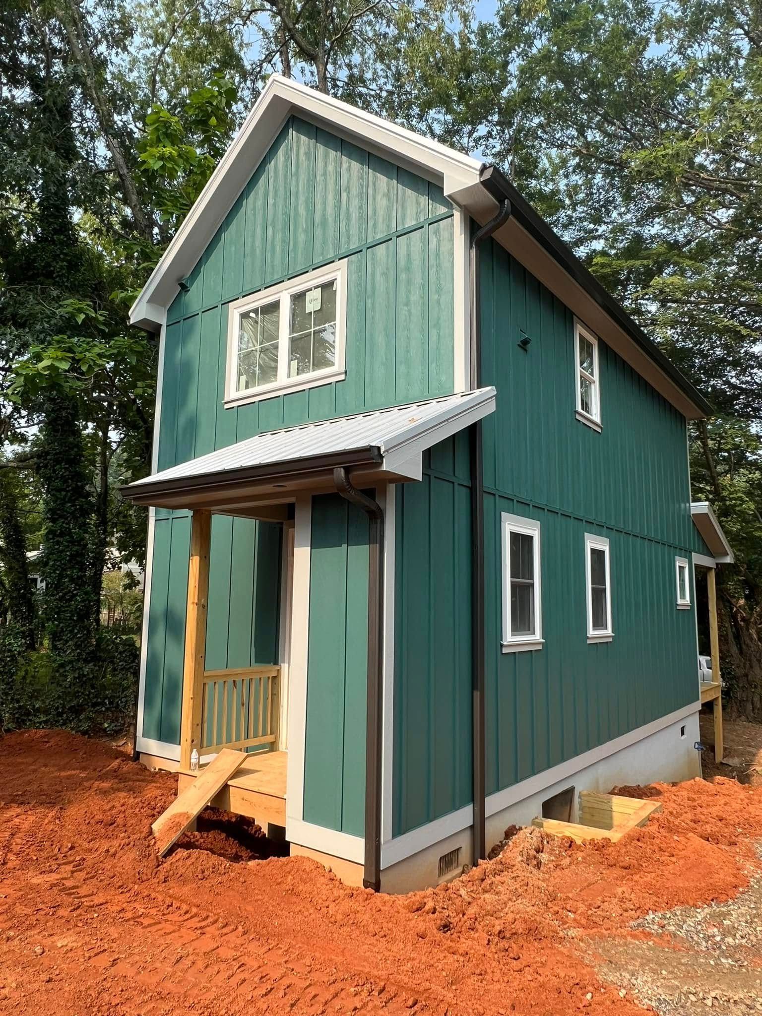 Teal two-story tiny house under construction with white trim and red dirt foundation