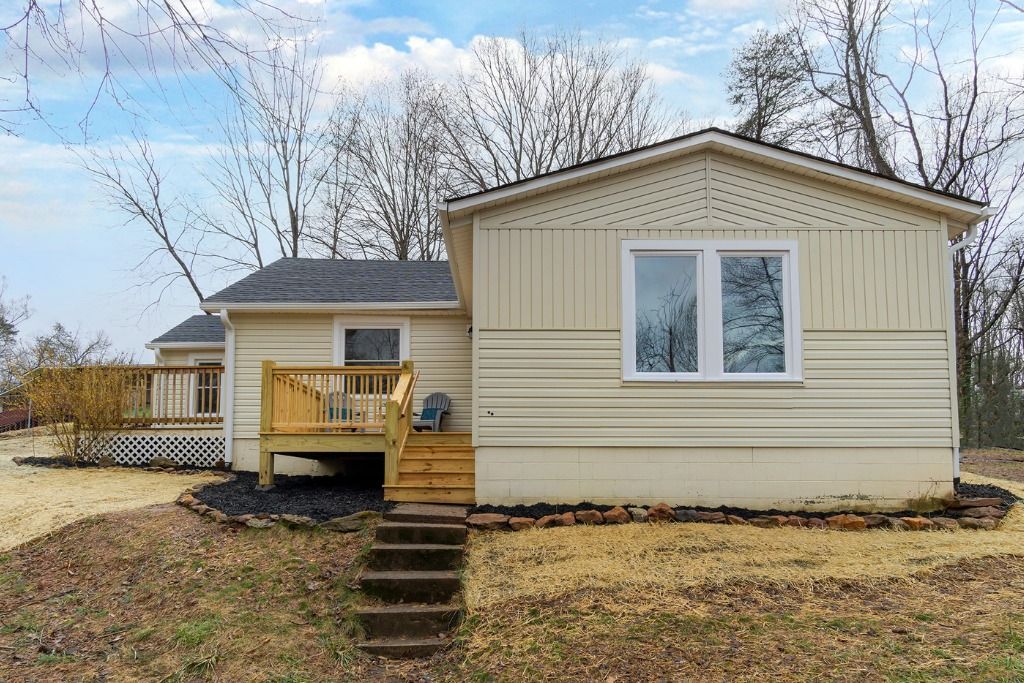 Single-story beige mobile home with a small wooden porch and steps in a grassy yard