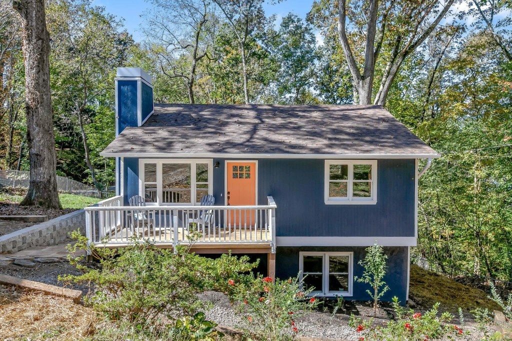 Blue house with white trim and front porch on a wooded hillside