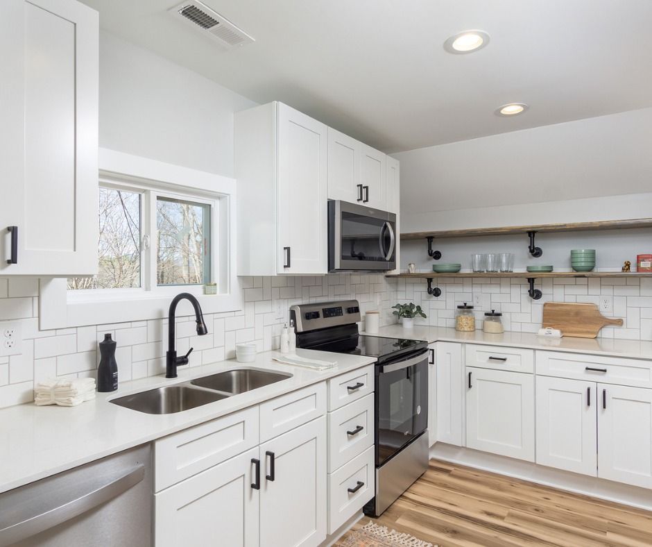 Bright modern white kitchen with stainless steel appliances, black fixtures, and wooden floorboards.