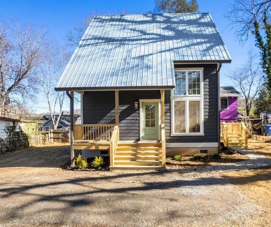 Small gray house with a steep metal roof, front porch, and steps in a sunny yard