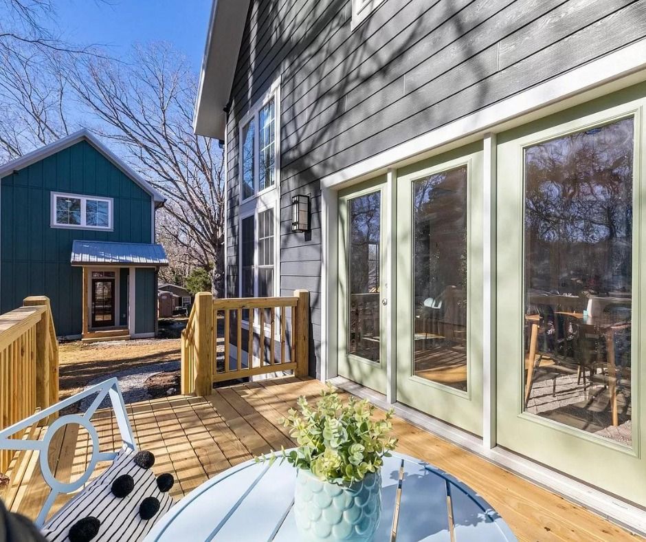 Back deck with white French doors, wooden railing, and blue house across a sunny backyard