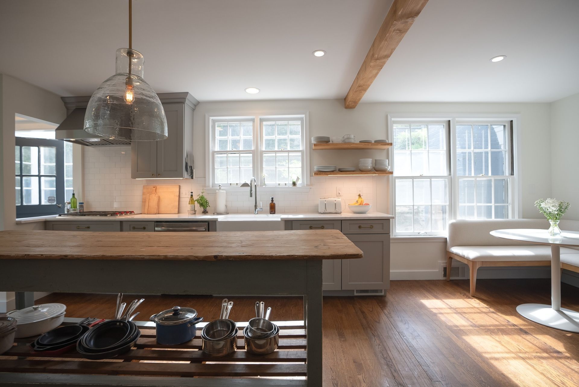 Bright modern kitchen with island, wood floors, hanging pendant light, and sunlit dining nook