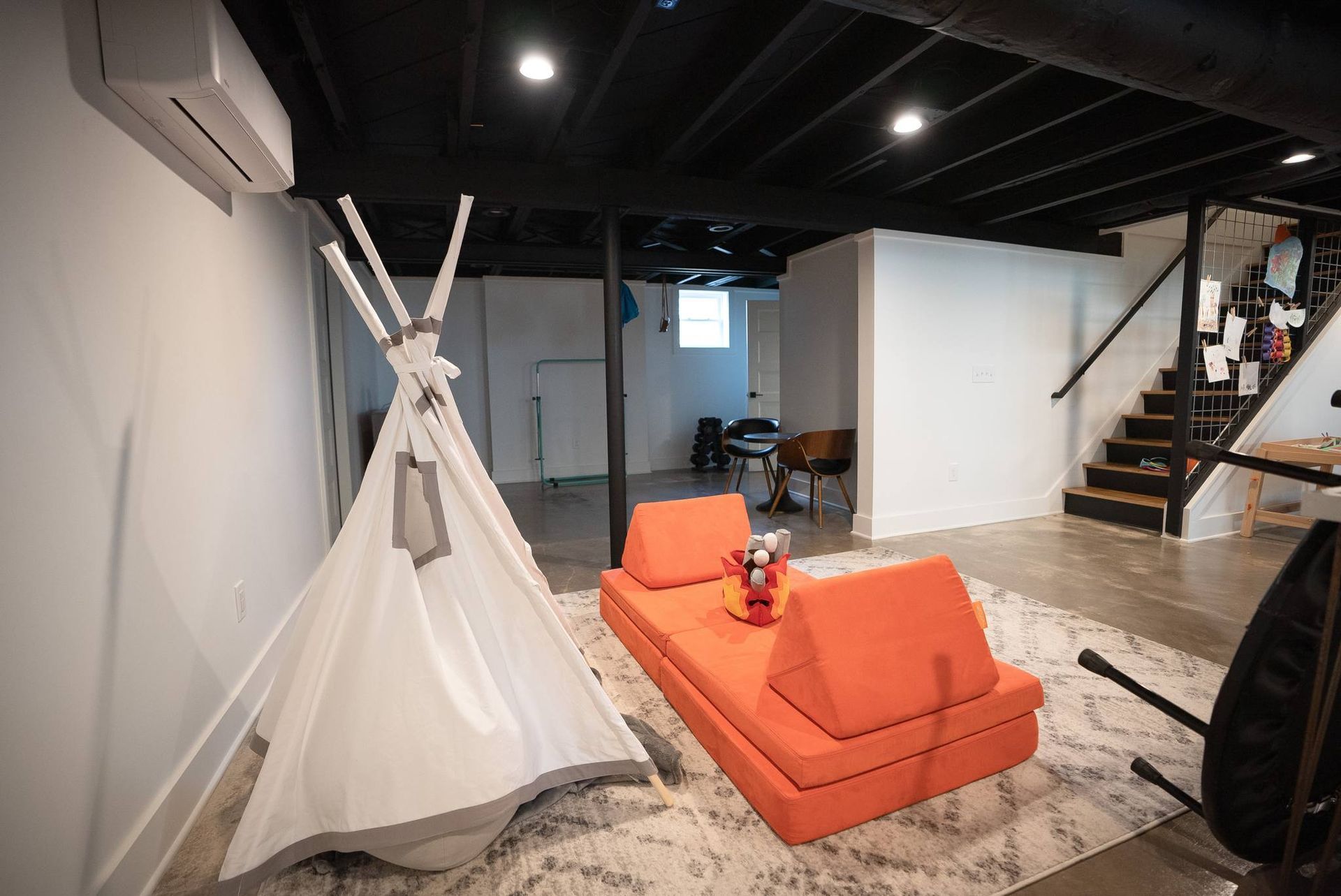 Modern living room with white teepee, orange sofa, and staircase under black ceiling lights
