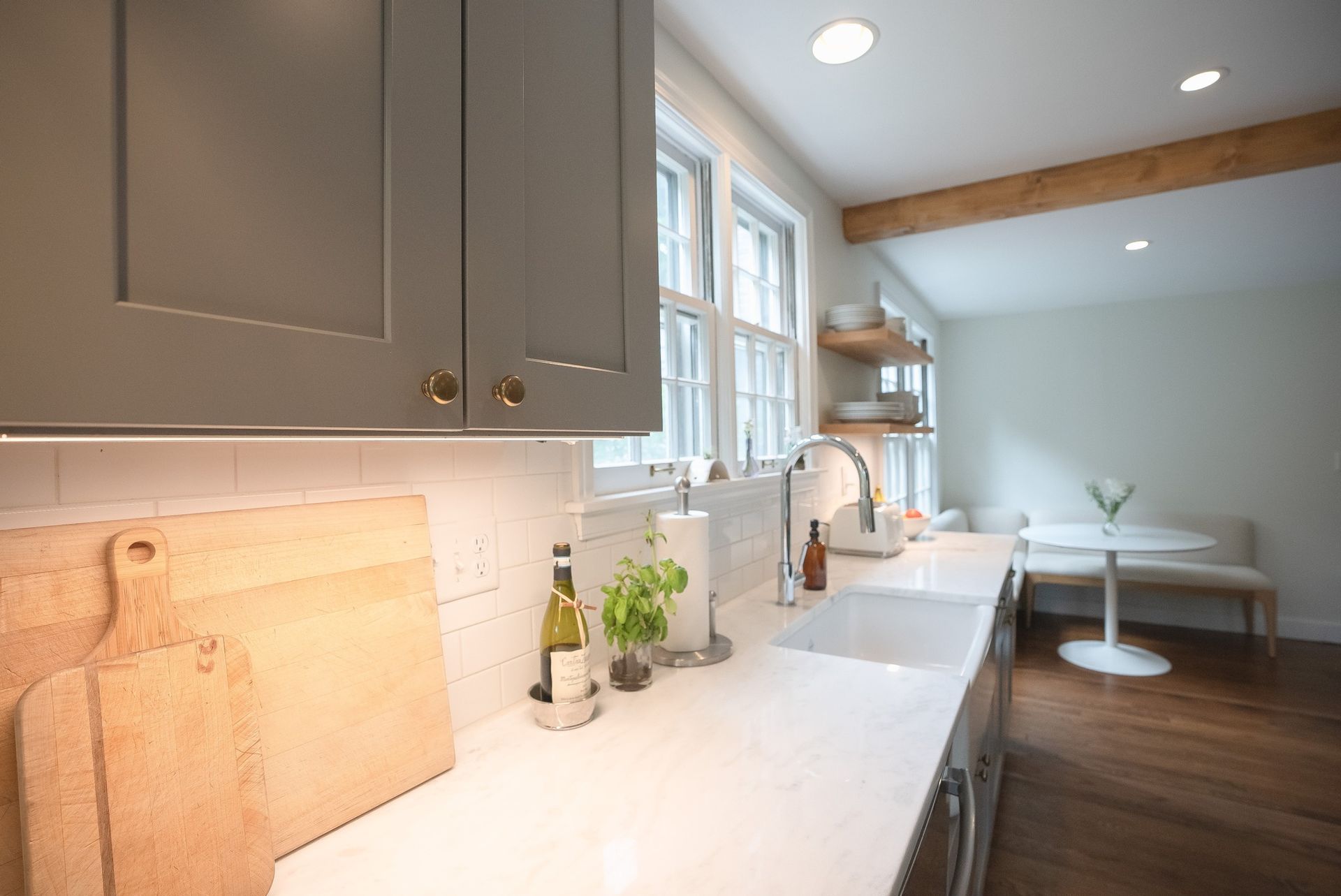 Bright modern kitchen with white countertops, gray cabinets, wood floors, and a dining nook by windows
