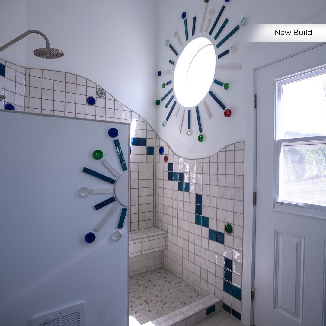 Bright tiled bathroom shower area with a frosted glass door and sunburst mirror above blue accent tiles.