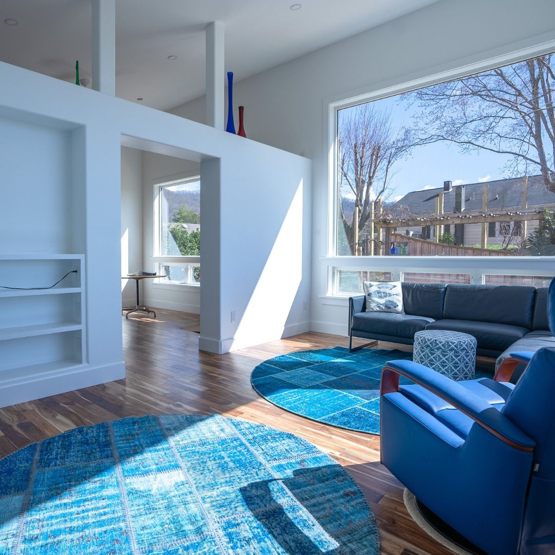 Bright modern living room with blue chairs, gray sofa, wood floors, and large sunny windows