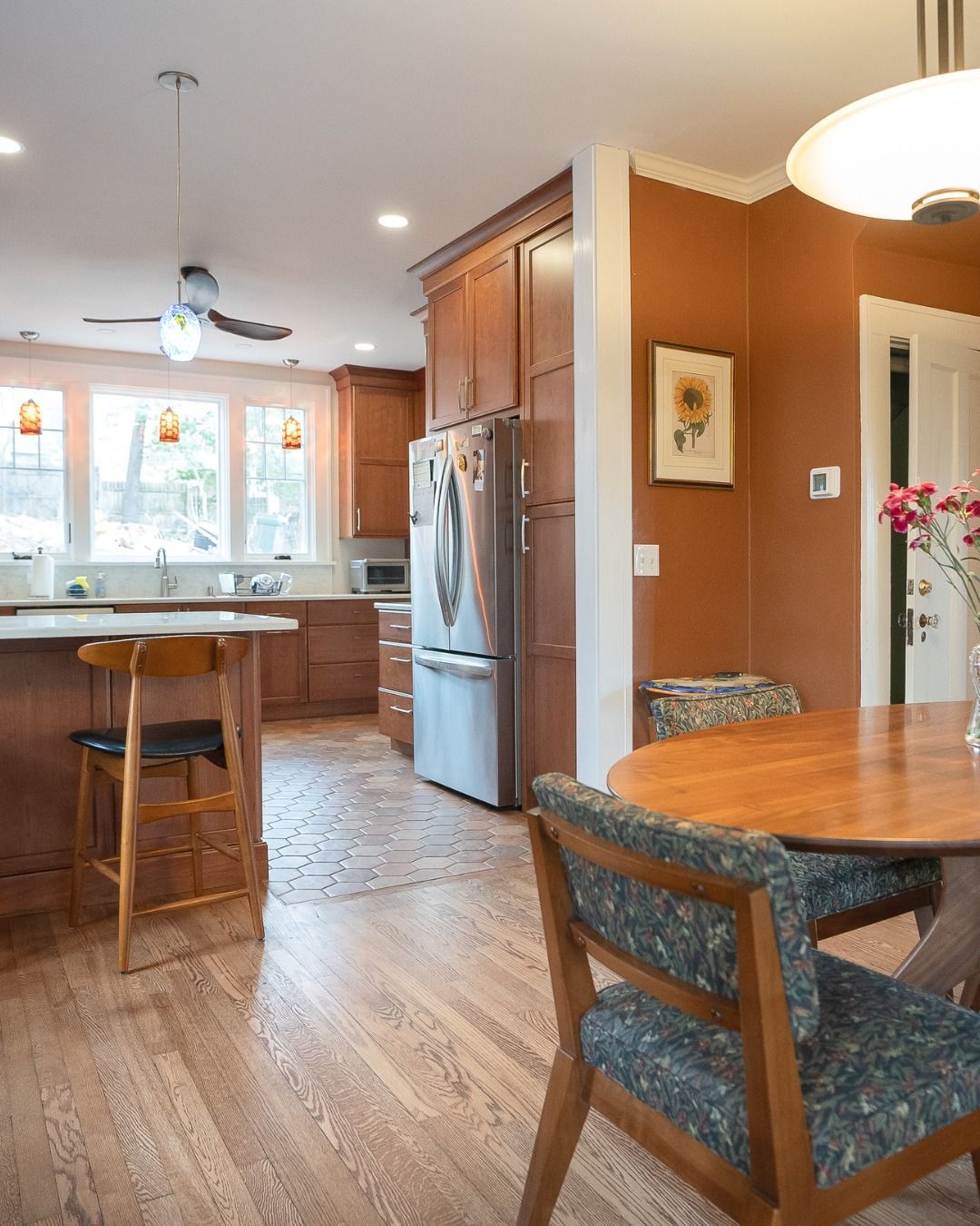 Bright kitchen with wooden floors, stainless fridge, island stools, and a dining table by a window.