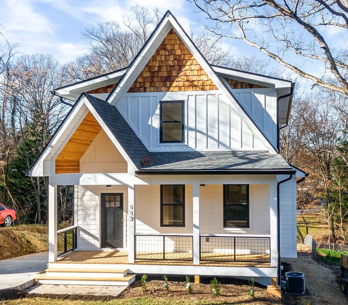 White two-story house with gray roof and wood gable, front porch, and bare trees in the yard