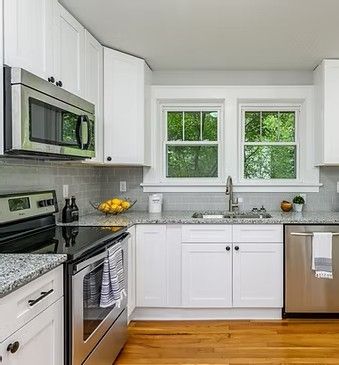 Bright white kitchen with stainless steel appliances, window over sink, and light wood floor