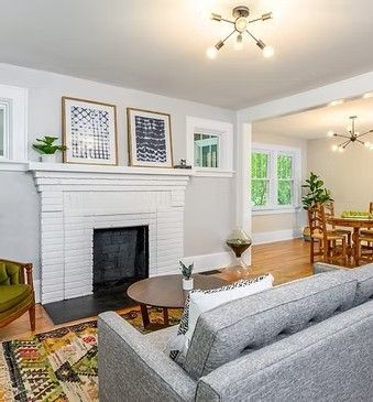 Bright living room with white fireplace, gray sofa, colorful rug, and dining area beyond to the right.
