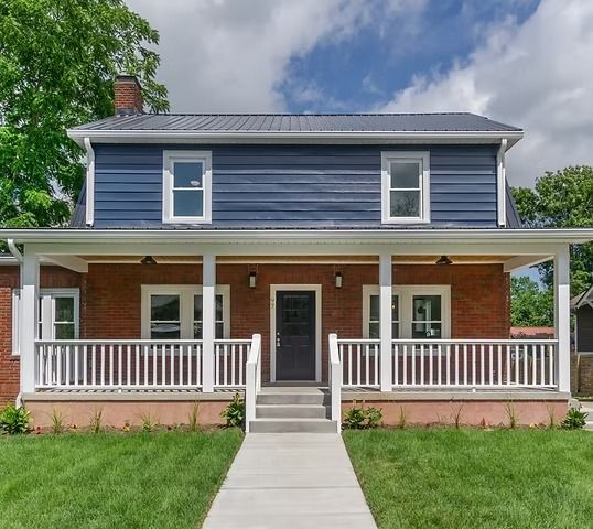 Front view of a brick house with a blue upper story, white porch railings, and a central walkway
