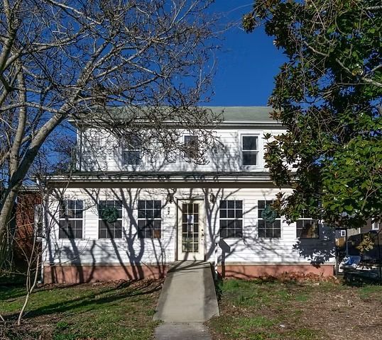 White two-story house with a front walkway, white porch railings, and leafless trees in front