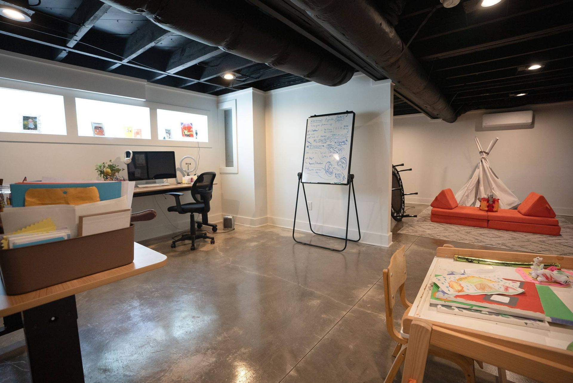 Open art studio with desks, whiteboard, easel, and colorful artwork on tables