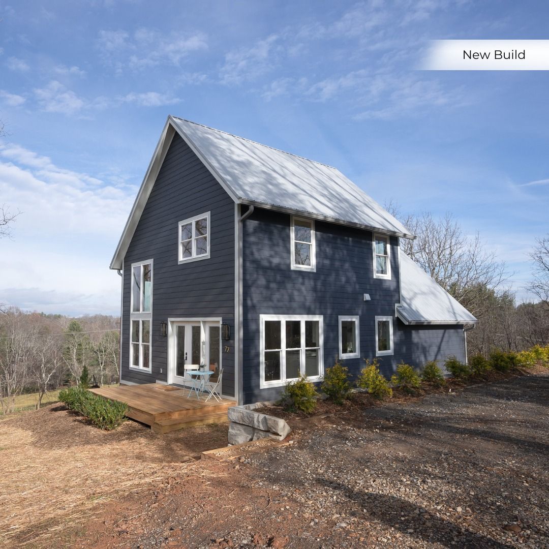 Blue two-story house with white trim and metal roof beside a gravel driveway under a partly cloudy sky