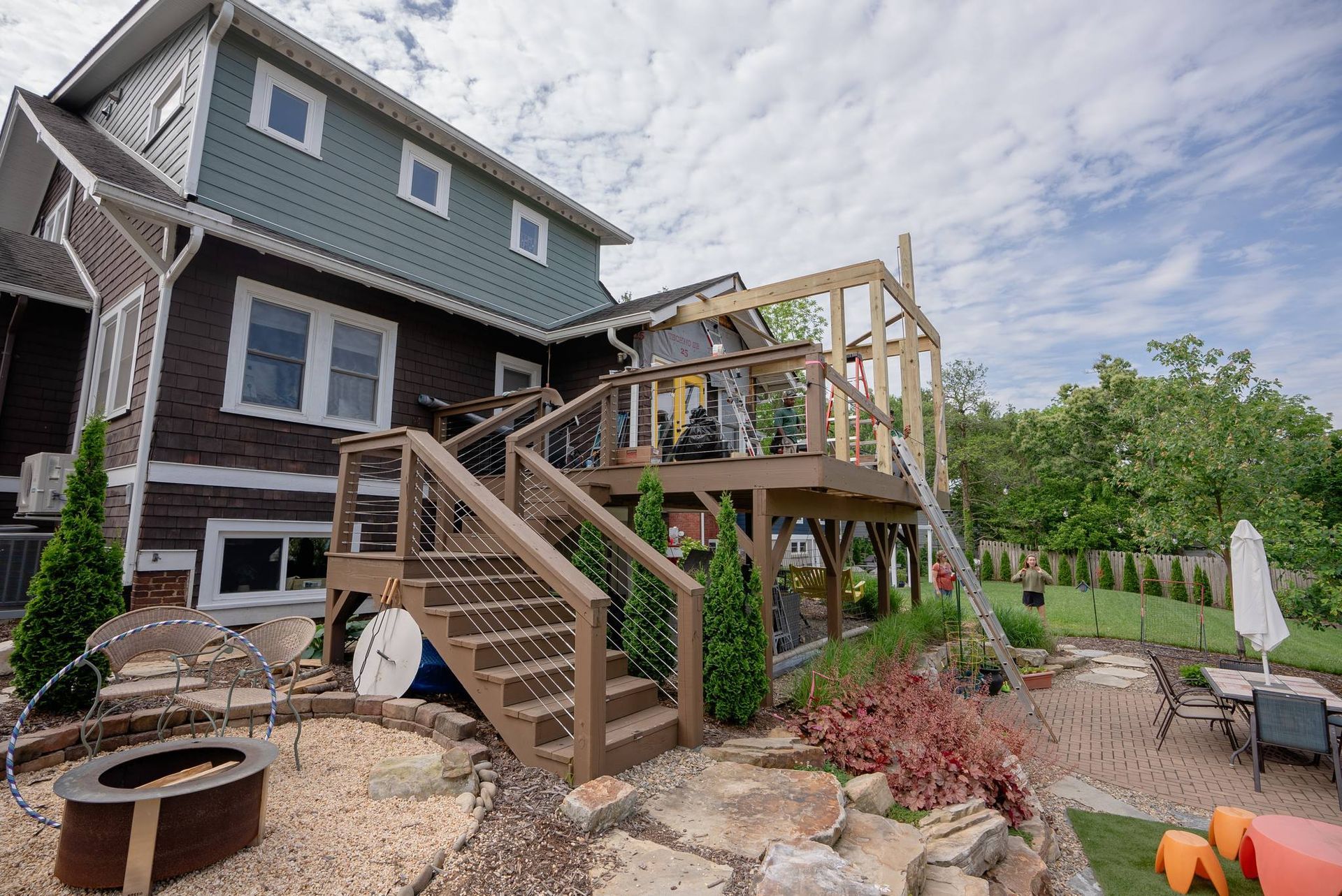 Backyard deck under construction beside a house, with stairs, railings, and a cloudy sky.