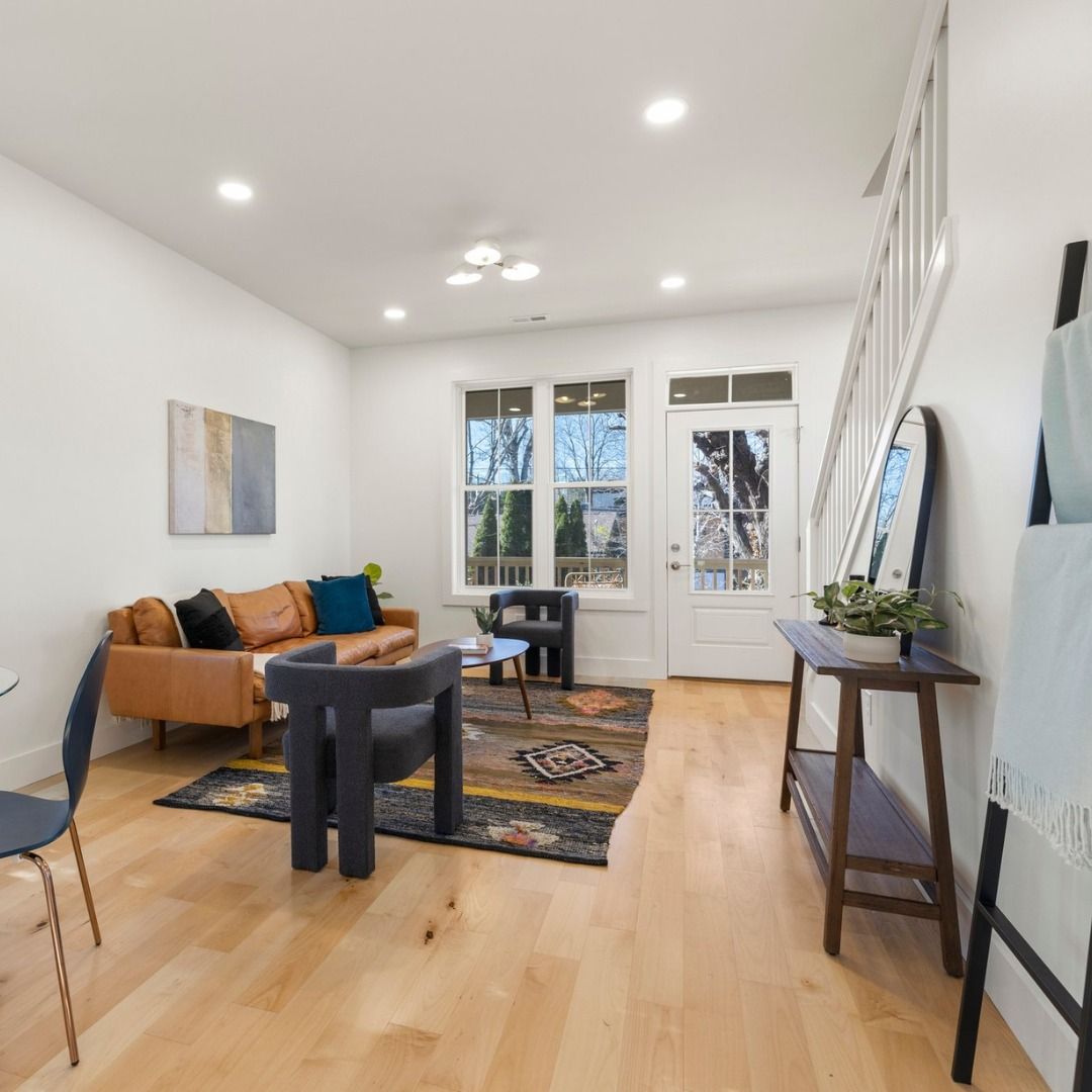 Bright living room with tan sofa, black table, patterned rug, and tall windows by a front door.