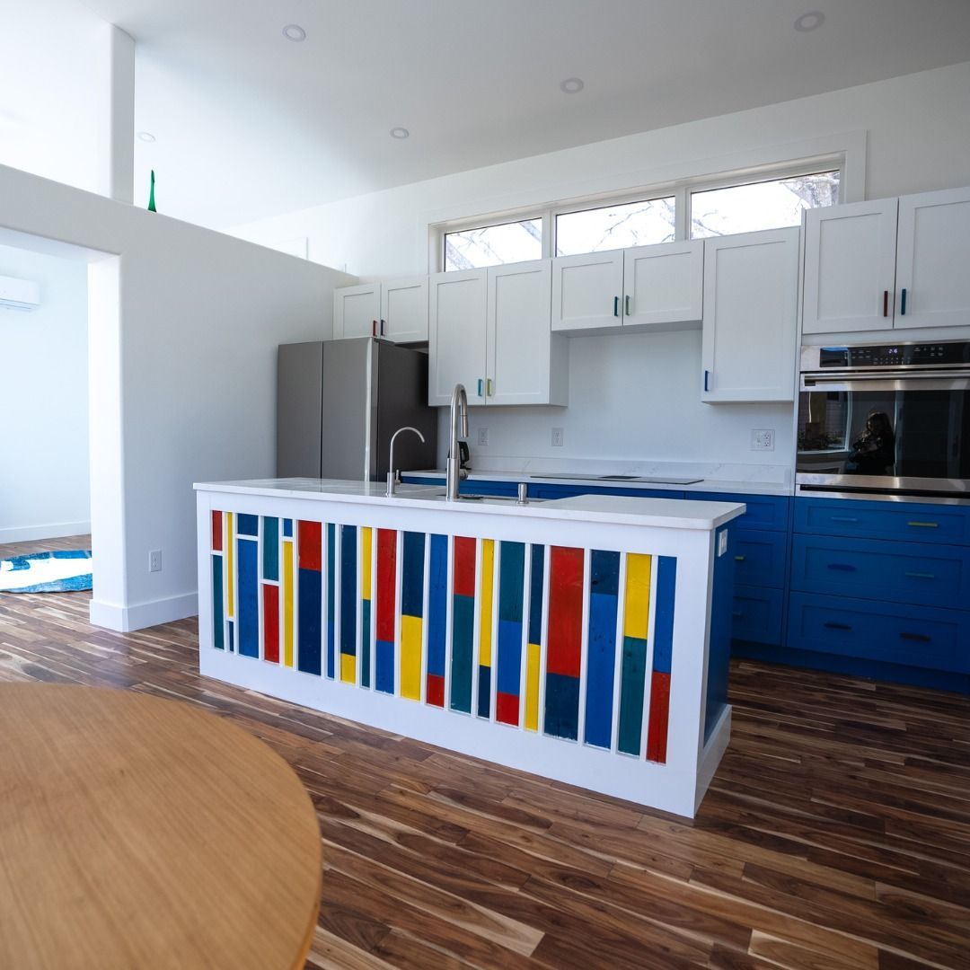 Bright modern kitchen with white cabinets, blue island base, colorful tile front, and wood floors