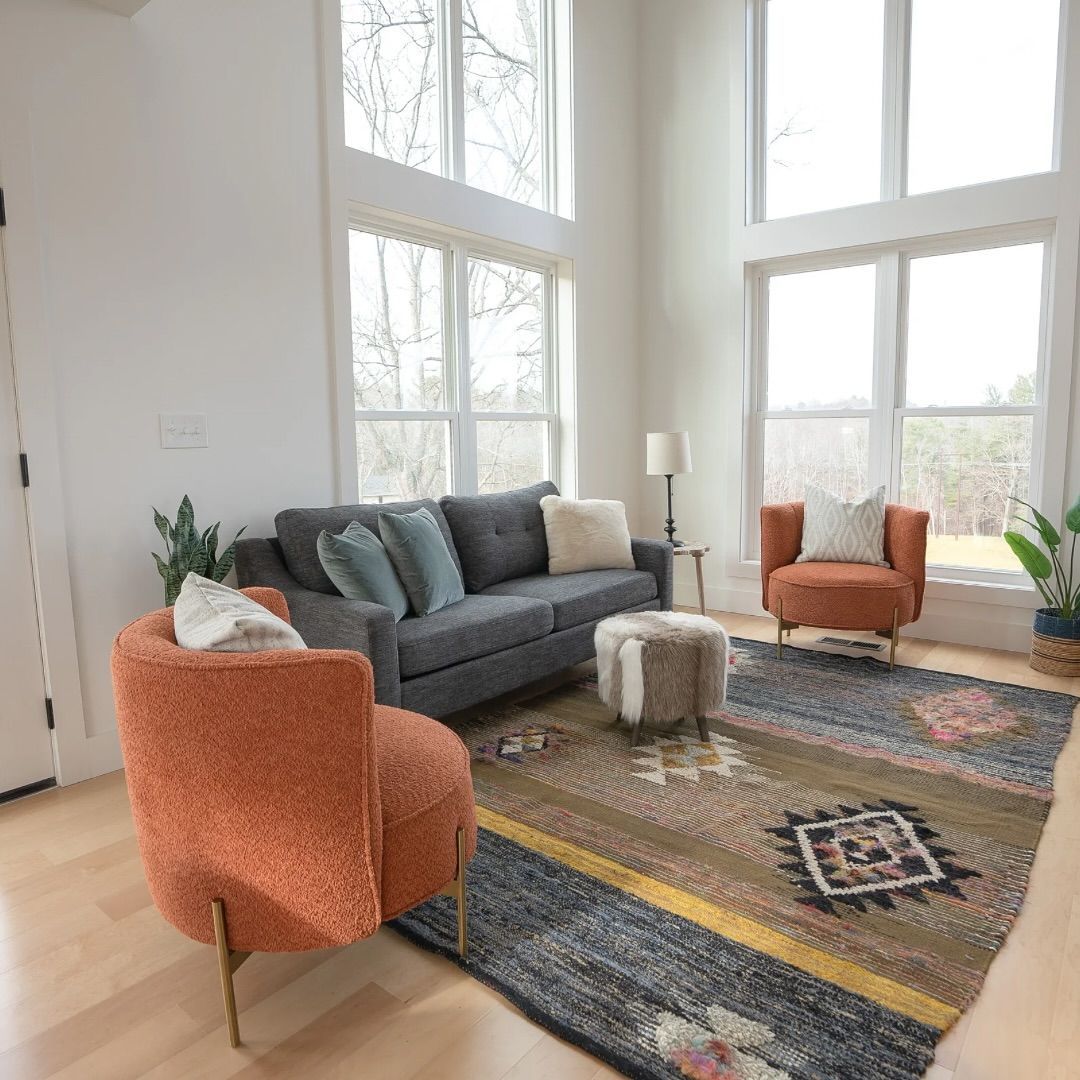 Bright living room with gray sofa, orange chairs, patterned rug, and large windows with natural light