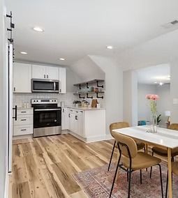 Bright modern kitchen and dining area with white cabinets, stainless steel appliances, and a wood table