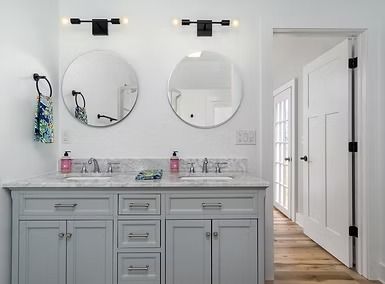 Modern white bathroom vanity with double mirrors, gray cabinets, and an open doorway to a hallway