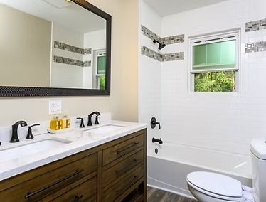 Modern bathroom with double vanity, large mirror, tiled shower wall, and toilet рядом
