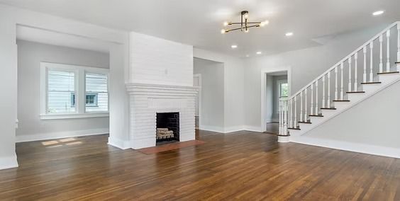 Bright empty living room with white walls, wood floors, fireplace, and staircase to the right