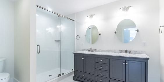Bright modern bathroom with glass shower, double vanity, mirrors, and dark gray cabinets