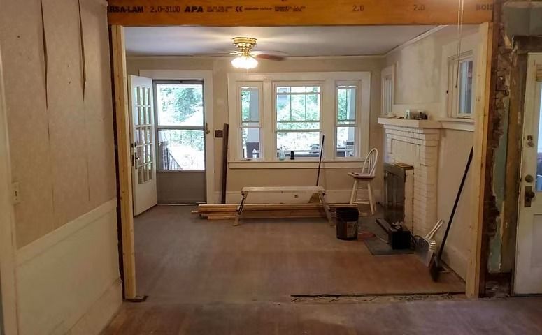 Empty living room with bare floor, fireplace, windows, and a bench by the front door