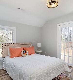 Bright bedroom with a white bed, coral pillows, and glass doors opening to a deck.