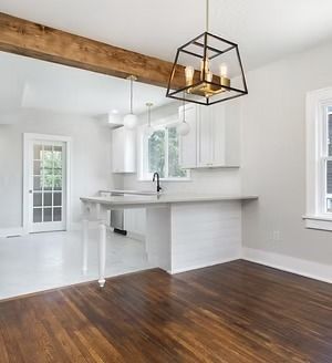 Bright white kitchen with exposed wood beam, dark hardwood floor, and modern black pendant light